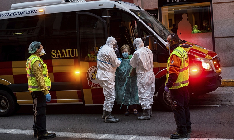 Hai nhân viên y tế đỡ bệnh nhân xuống xe cứu thương ở thành phố Madrid hôm 24/3. Ảnh: AP.