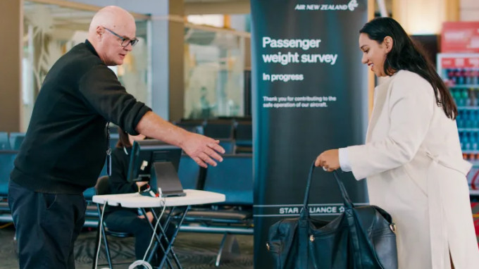 Một người phụ nữ đưa túi cho nhân viên để cân trước chuyến bay ở Auckland, New Zealand ngày 29/5. Ảnh: AP
