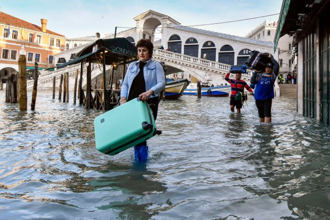 Khách du lịch xách hành lý lội qua nước lũ ở Venice ngày 23/12/2019. Ảnh: AP