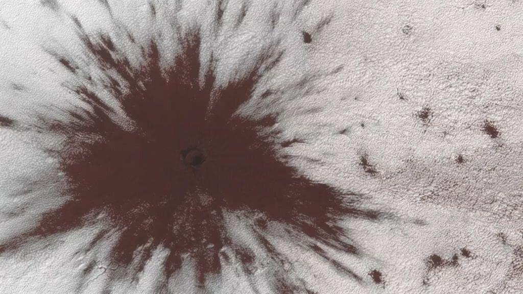 Vào khoảng giữa tháng 7 và tháng 9/2019, vật thể không gian - có thể là sao băng hoặc mảnh sao chổi – va vào chỏm băng phía Nam của sao Hỏa và chọc thủng lớp băng mỏng, bắn ra trận mưa bụi nâu đỏ tung tóe. Kết quả là mảng màu nâu đỏ sẫm hiện ra trông giống như cảnh tạo ra khi nhân vật hoạt hình chạy đâm thẳng vào tường. Bức ảnh do tàu quỹ đạo trinh sát sao Hỏa của NASA chụp lại, và vệt bụi nâu đỏ tung tóe này có chiều ngang khoảng 1km. (Ảnh: NASA/JPL/Đại học Arizona)