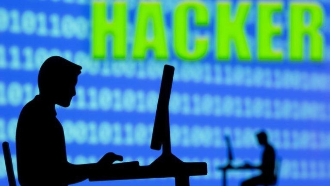 Một mô hình người dùng máy tính, phía sau là hình nền có nội dung về hacker. Ảnh: Reuters