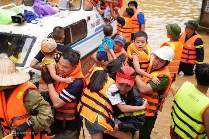 Trẻ nhỏ được đưa lên ca nô rời khỏi vùng ngập lụt. Ảnh: Nguyễn Đông