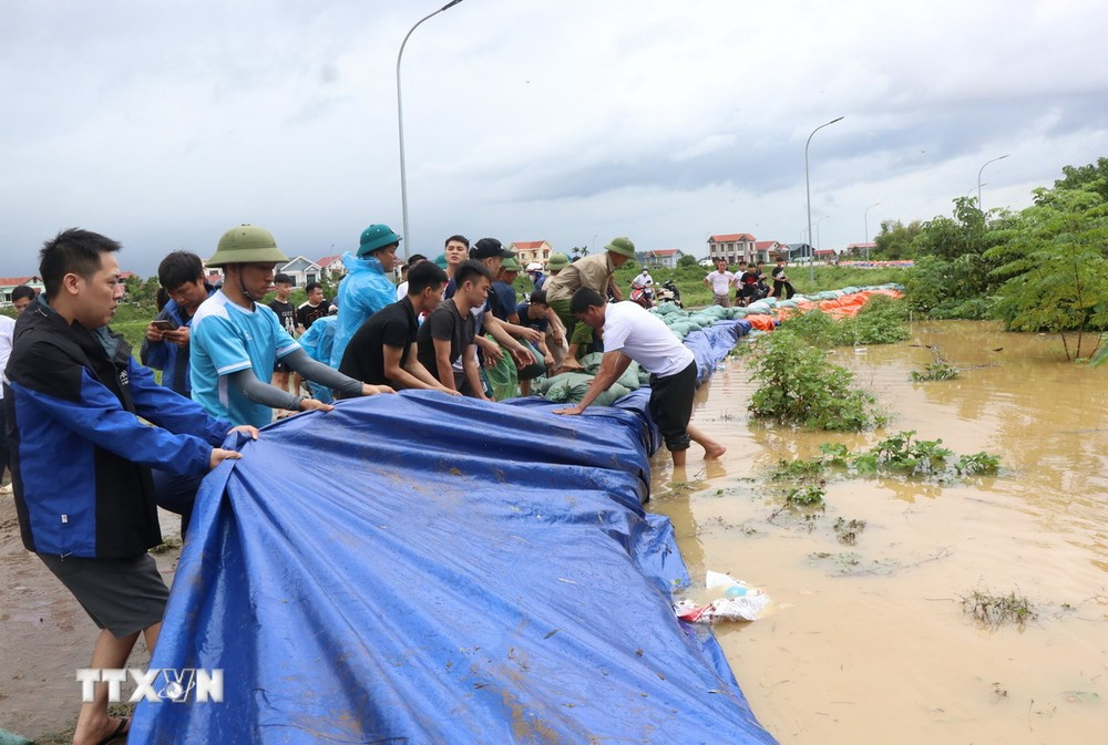 Người dân tích cực đắp cát, bạt qua đê để ngăn lũ. (Ảnh: Thanh Thương/TTXVN)