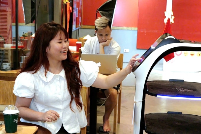 Bạn Hà Phương (Hà Nội) tương tác với robot bưng bê - nhân viên phục vụ của cửa hàng cà phê tương lai. Ảnh: Lộc Chung
