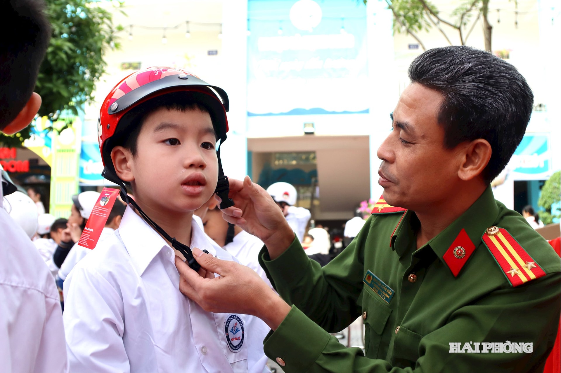 Anh bao in: Cán bộ Công an phường Lê Chân cài mũ bảo hiểm cho học sinh nhà trường.