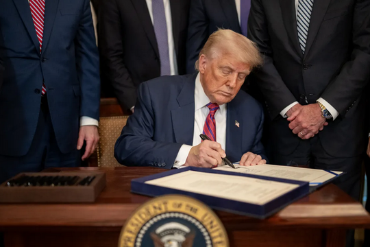 президент США подписывает документ, на заднем плане флаг